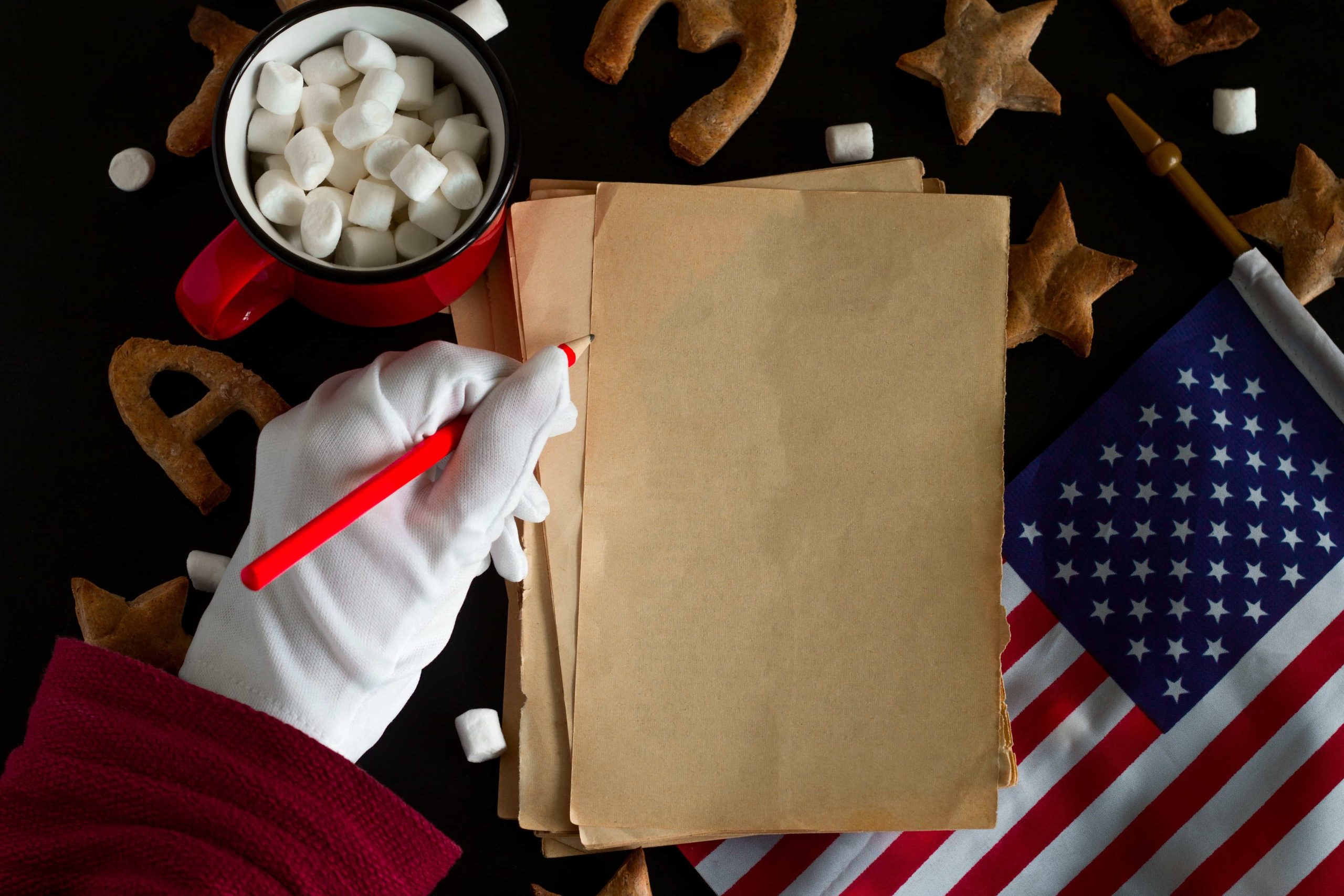 Santa's gloved hand writing a personalized letter with cookies, cocoa, and holiday decor nearby