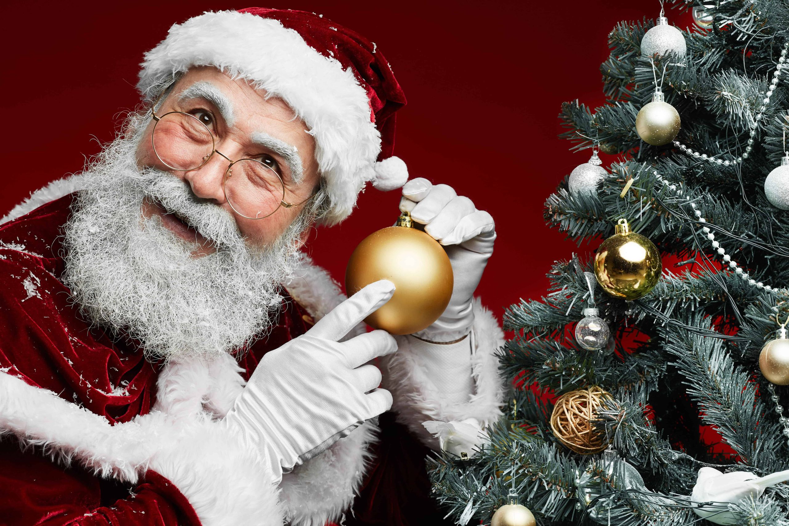 Santa Claus decorating a Christmas tree with a gold ornament